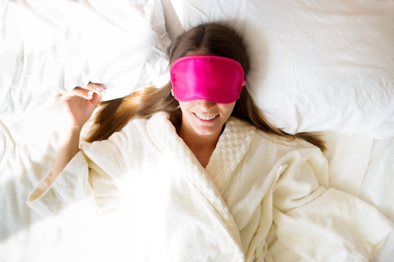 Beautiful brunette girl lies in bed in a mask for sleep.